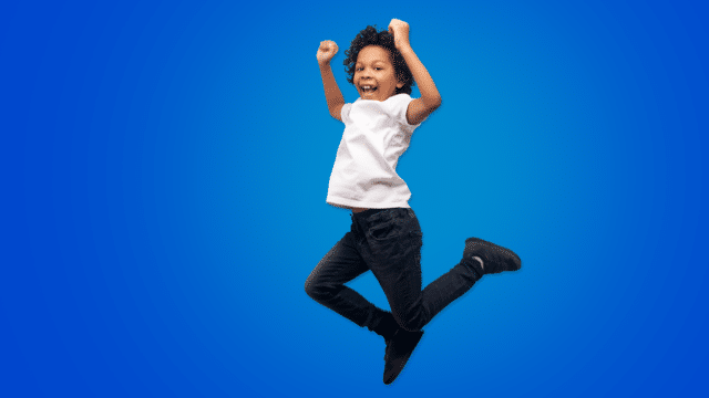 A child dressed in a white shirt and black jeans jumps in front of a blue background.