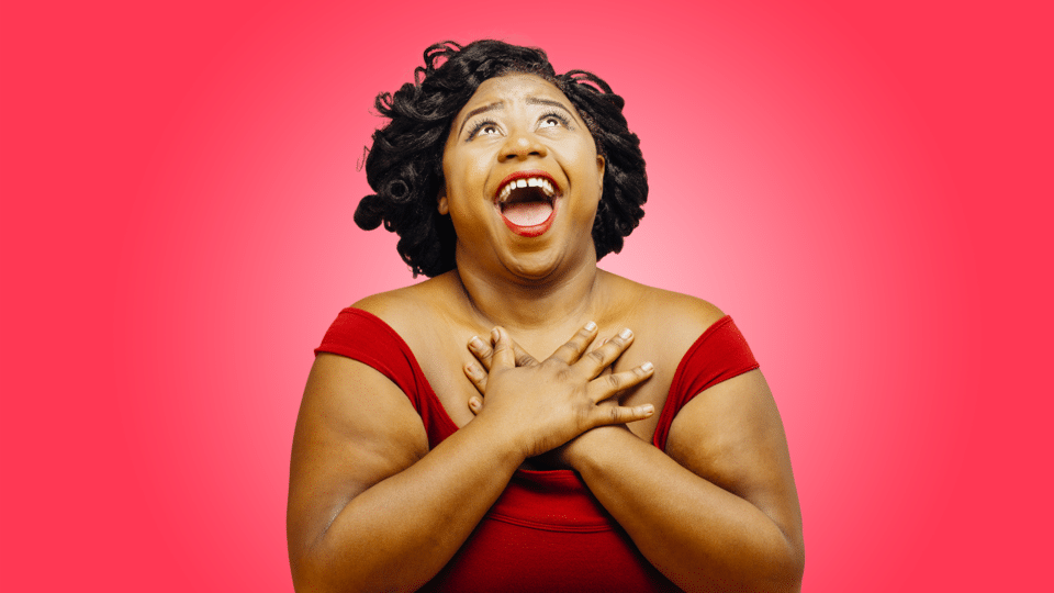 Community Choir - photo of a lady in a red dress, looking up singing with her hands on her chest on a red background