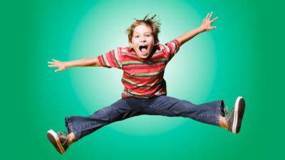 MYC 8-11s Image - Photo of a boy jumping in the air with his arms and legs outstretched on a green coloured background.