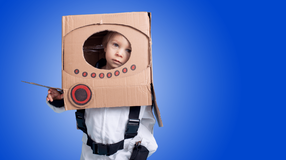 Tots Stars - photo of a young boy dressed as a space ship with a cardboard box on his head on a blue coloured background.