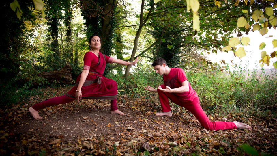 Two people in red outfits dance in a forest.