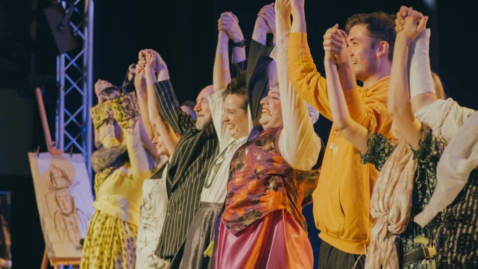 The whole cast of the show holding each other’s hands in unison