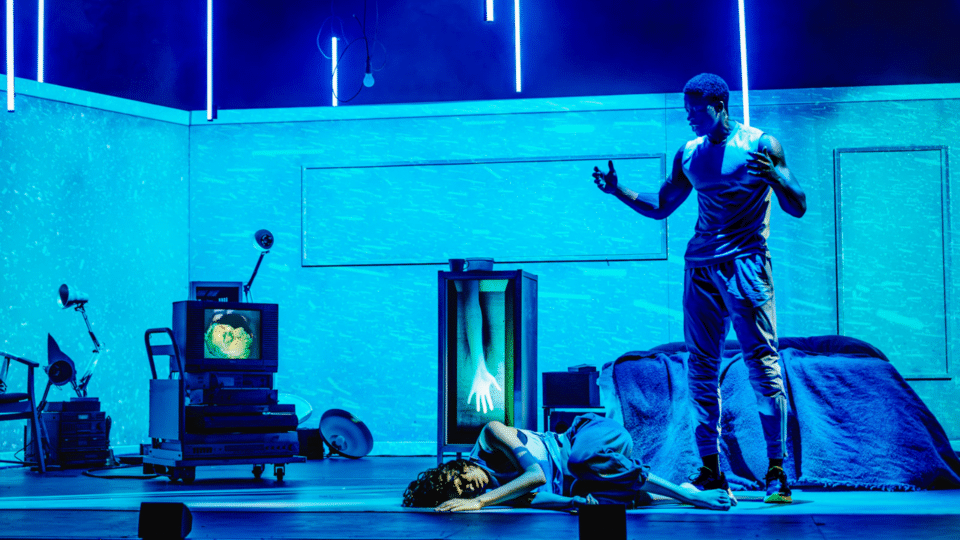 two actors, one of them lying on the floor while the other is standing and looking down