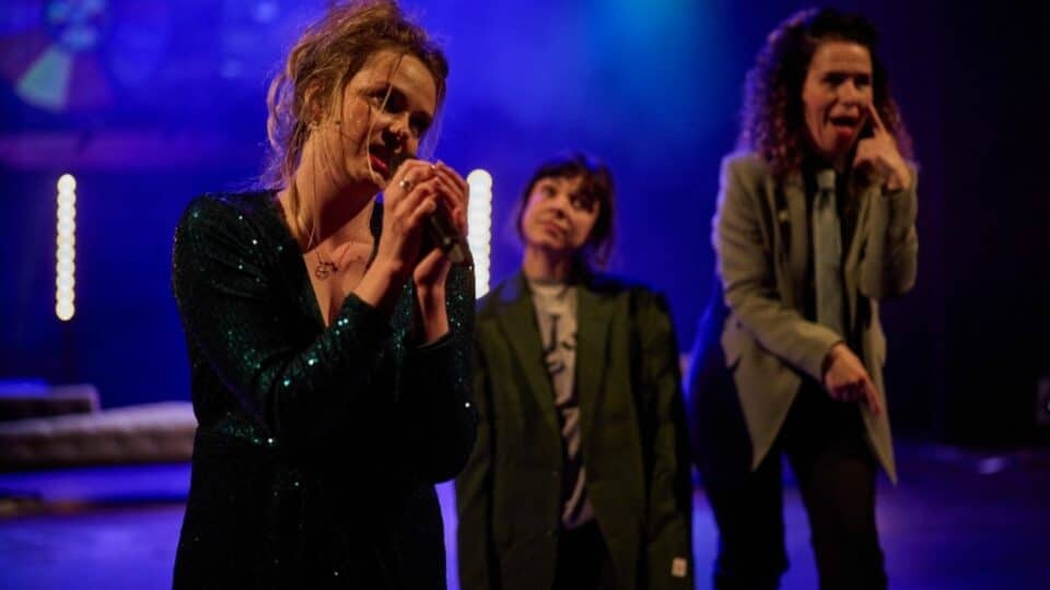 Three women performing while one of them is holding a microphone
