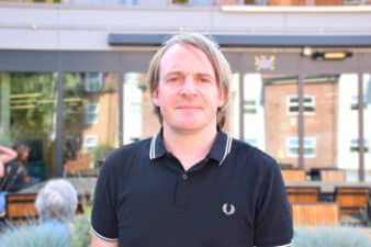 A photo of Kenny Emson, a white man with grey hair, smiling outside the Mercury Theatre